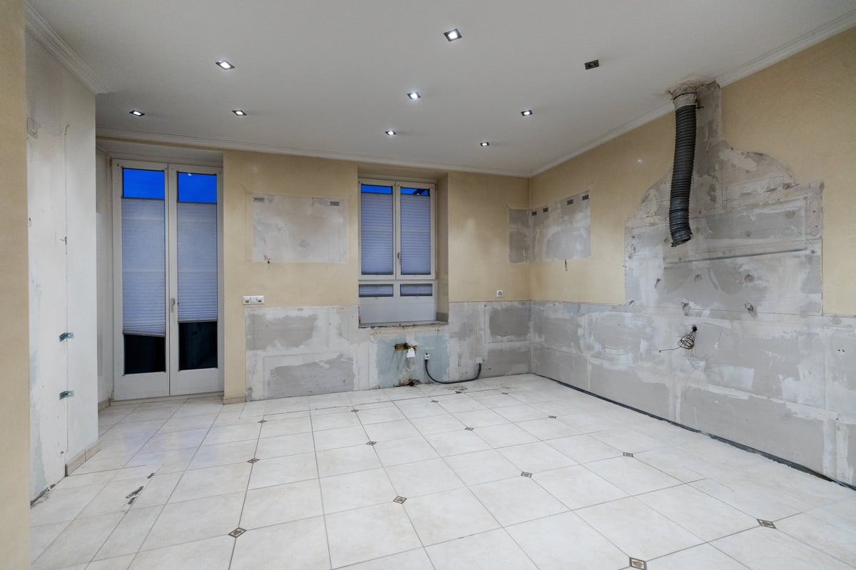 Empty kitchen under renovation with bare walls, tile flooring, recessed lighting, and glass doors leading to a balcony