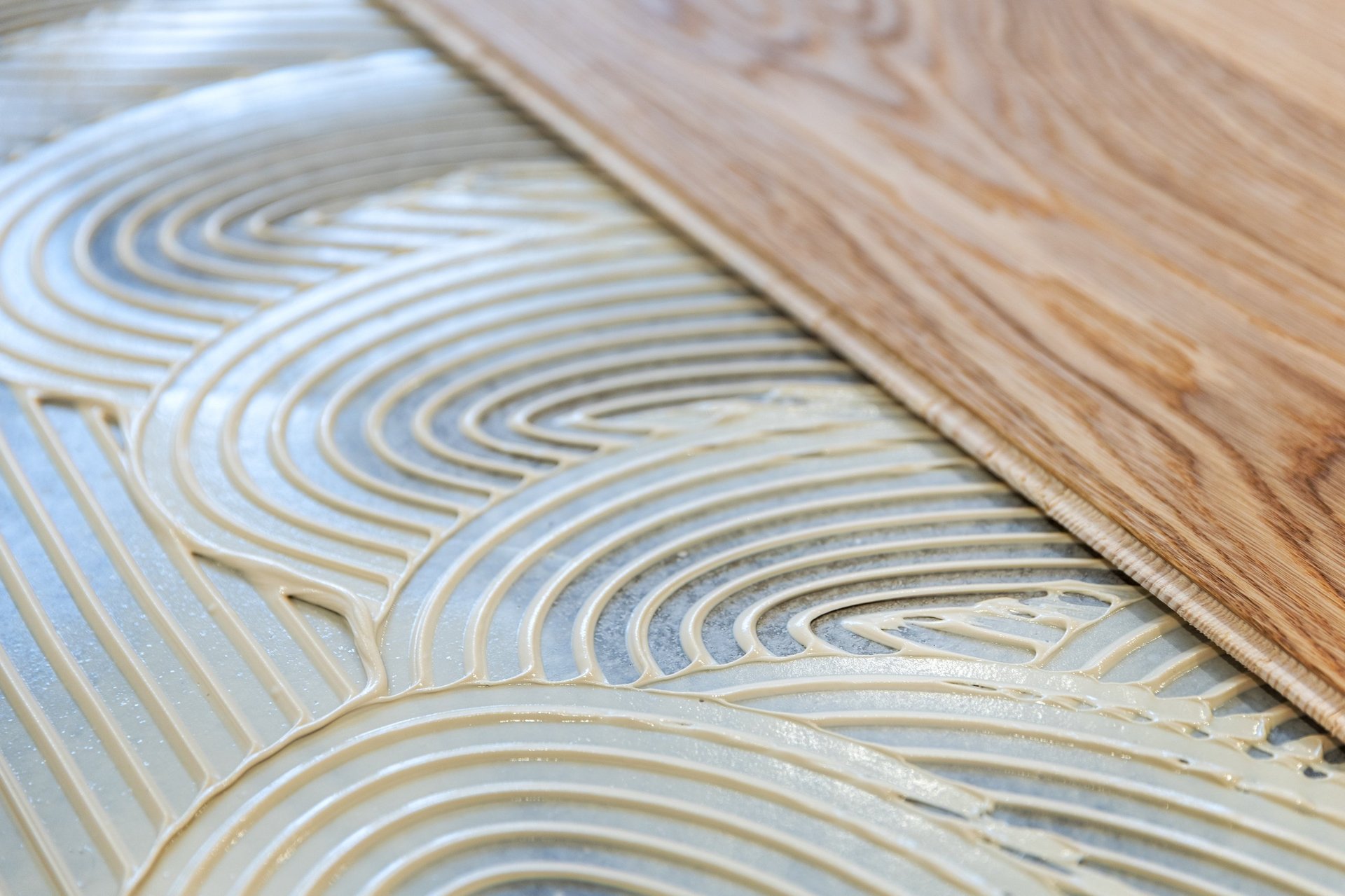 Close-up of thin-set mortar with wavy trowel lines and wooden flooring edge above