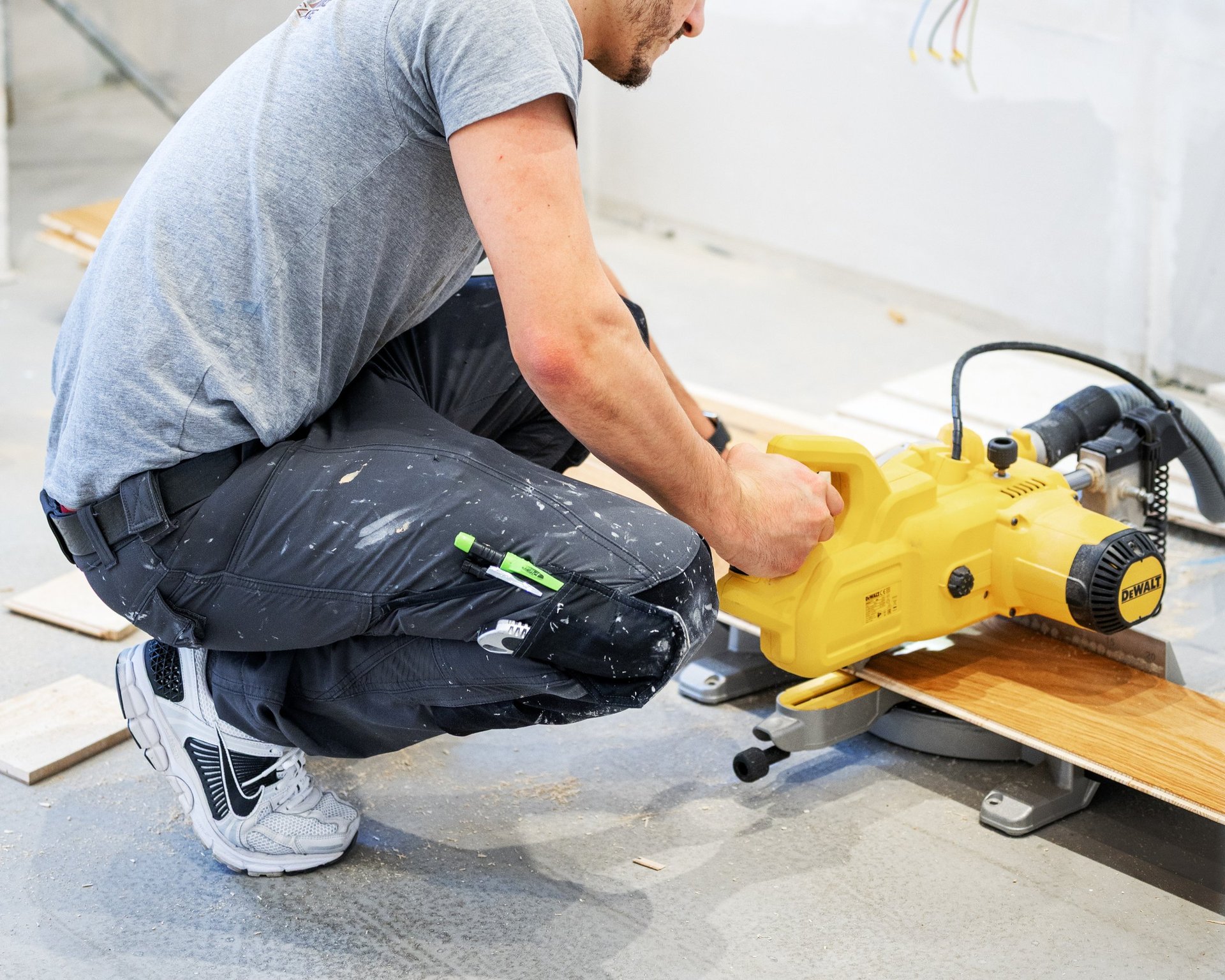 Man using a yellow power planer on a wooden board during construction work indoors