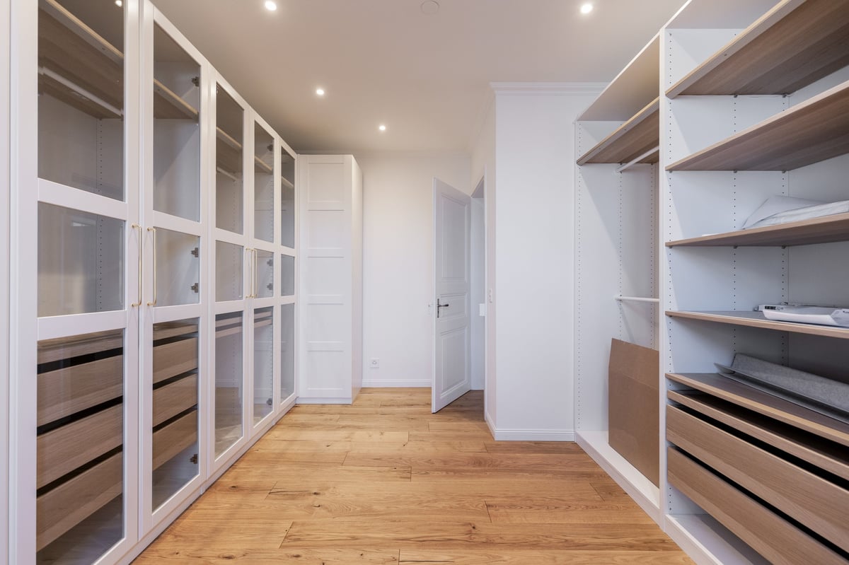 Modern walk-in closet with white framed glass cabinets, wooden shelving, and hardwood floors