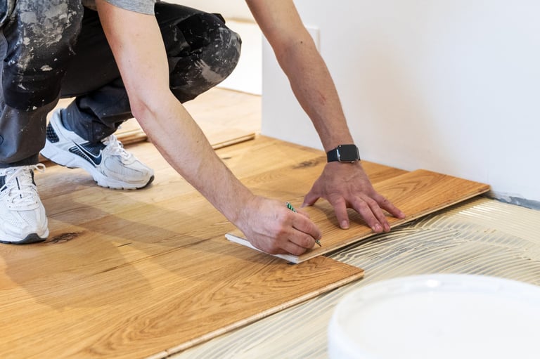 Worker installing laminate flooring by hand, pressing down planks on adhesive subfloor