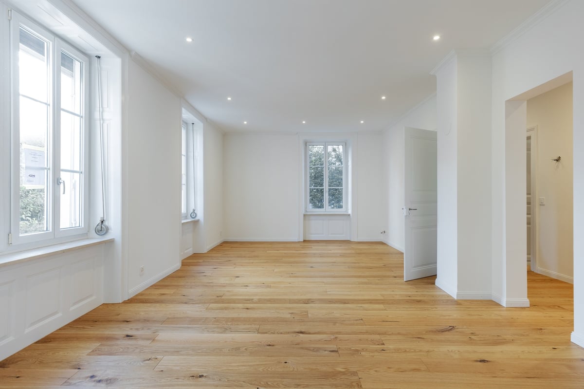 Empty bright room with wooden floor, white walls, large windows, and multiple doorways