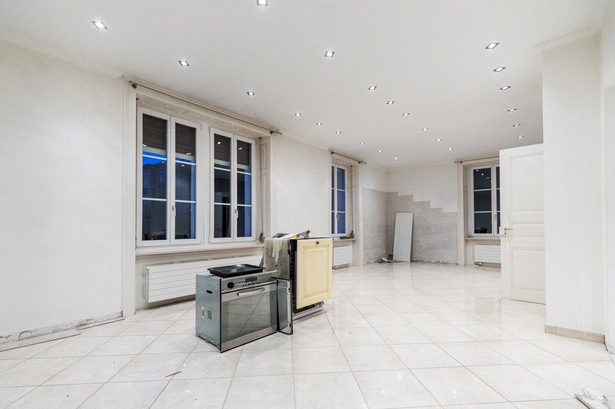 Empty unfurnished apartment interior with white walls, tile flooring, windows, and construction materials