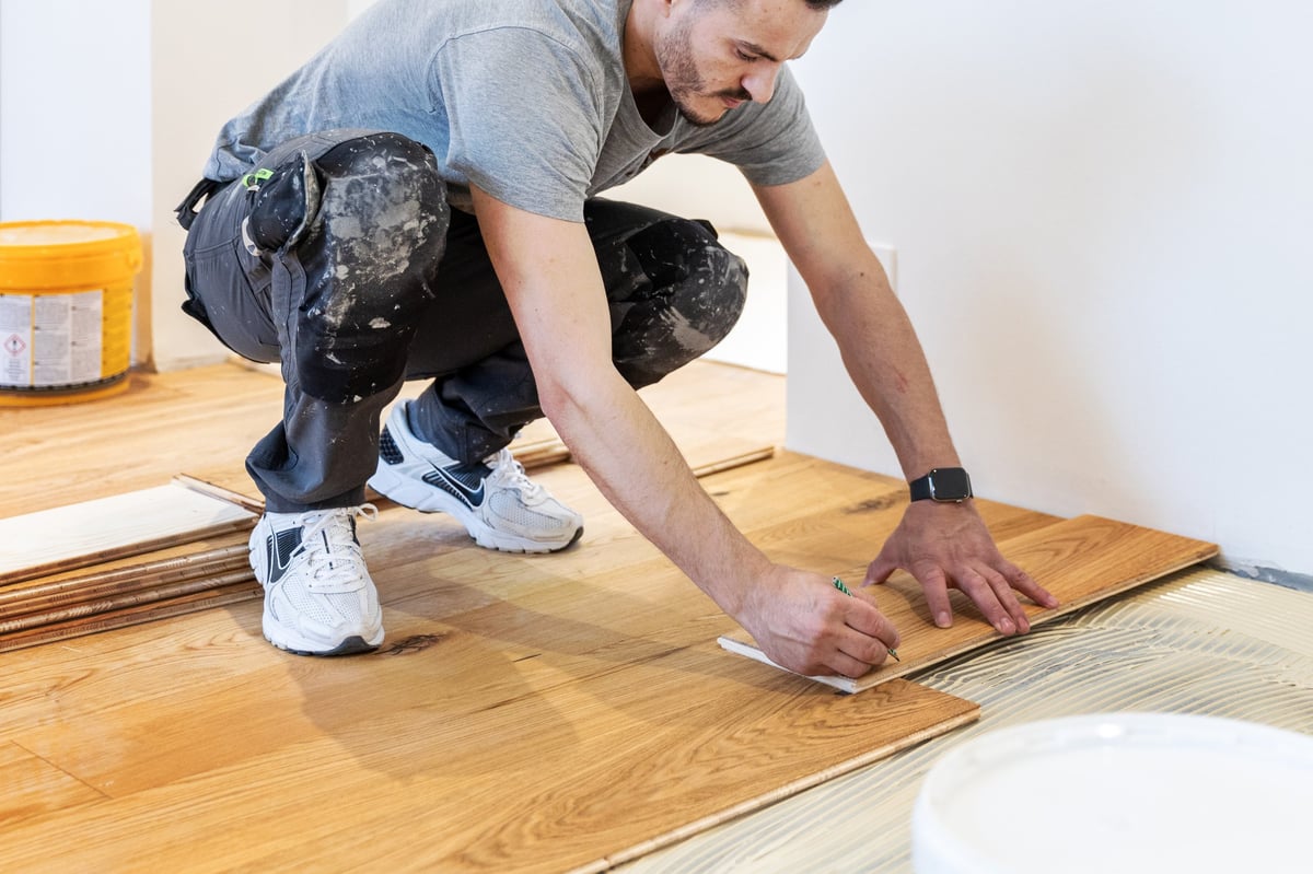 Worker installing hardwood flooring in an interior room, using tools and pressing wooden planks into place